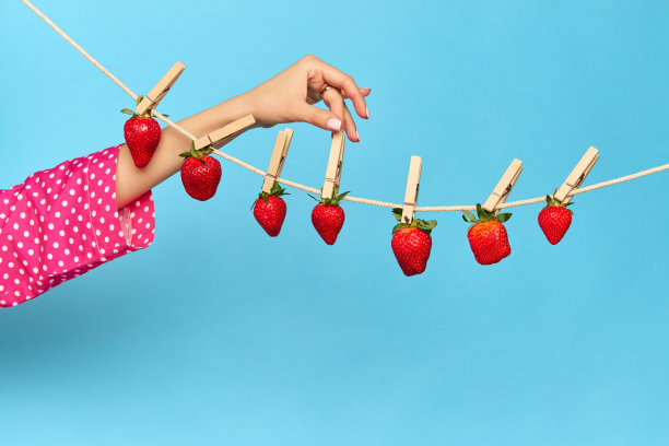 创意肖像与新鲜的草莓悬挂和干燥的绳子在蓝色的工作室背景。多汁水果排毒图片下载