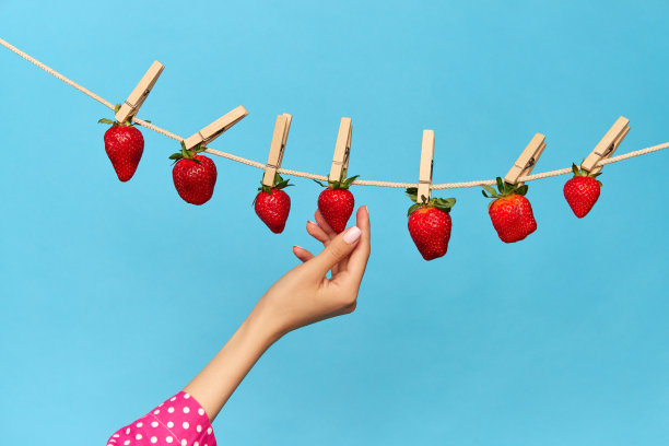 创意肖像的美味草莓挂和干燥的绳子在蓝色的工作室背景。有机农场食品图片下载