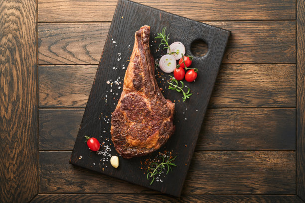 Tomahawk牛排。切成薄片的烤战斧式牛排，配上烤过的圣女果、香草和盐。准备烧烤。俯视图和复制空间。图片下载