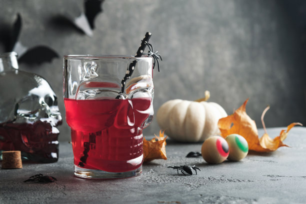 万圣节血腥鸡尾酒。万圣节的血红色鸡尾酒酒杯和黑色背景的瓶子形状的头骨。有糖果眼睛，蝙蝠，蜘蛛的万圣节派对。亡灵之殇。Clous-up。图片下载