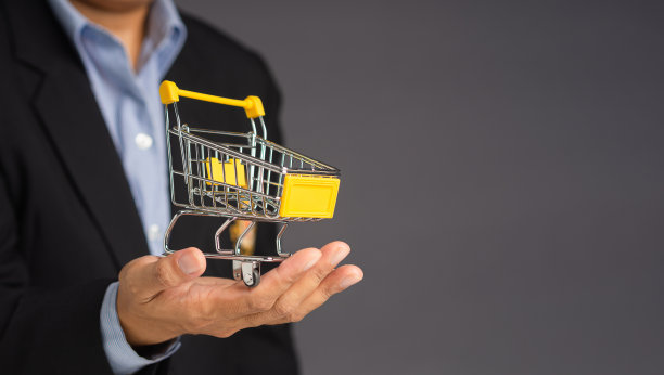 商人在灰色背景上展示一个迷你购物车。图片下载
