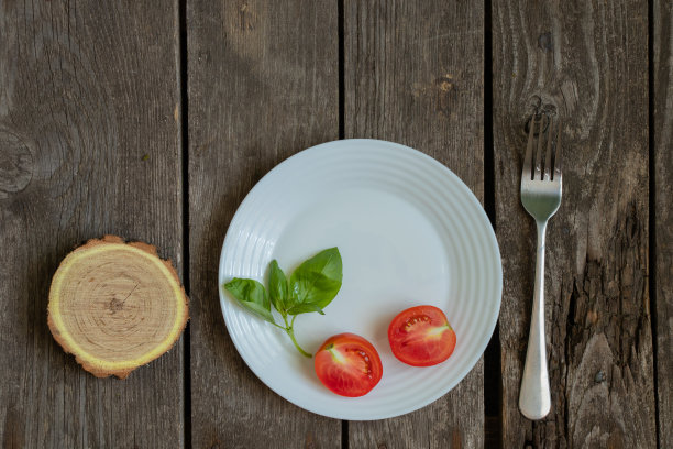 厨房里的一张旧桌子上放着一根罗勒花枝和一个西红柿，把空盘子和叉子清理干净图片下载