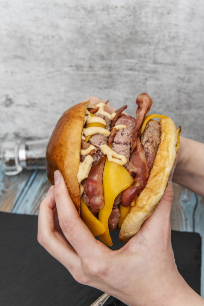 两只手拿着一个巨大的三肉牛肉汉堡，里面有很多煎培根和切达奶酪和酱汁图片下载