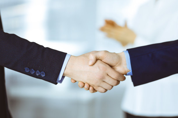 商务人士在会议或谈判中握手，特写。一群不知名的商人和一个女人站在一间现代化的办公室里。团队合作，伙伴关系和握手的概念图片下载