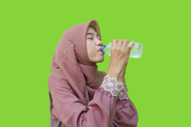 穆斯林妇女喝着绿色背景的瓶装水图片下载