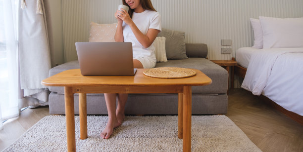 一个年轻女子在家里边喝咖啡边用笔记本电脑工作的特写图片下载