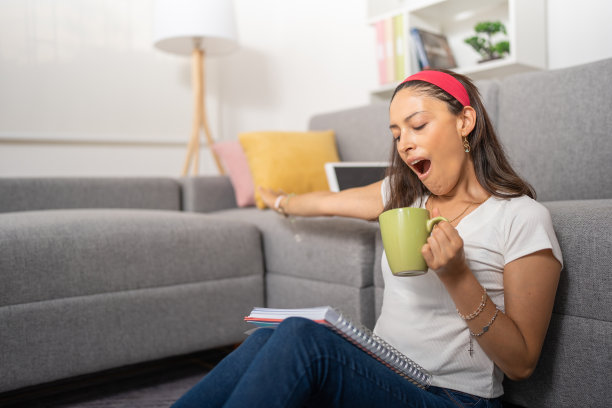 年轻的女学生，打着哈欠，喝着咖啡，看着她的笔记本图片下载