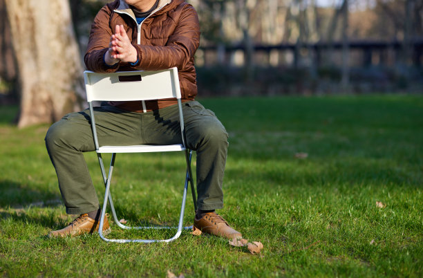 一个男人坐在草坪上的白色折叠椅上图片下载
