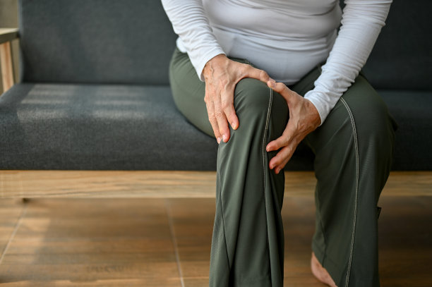 一位上了年纪的妇女，抱着膝盖坐在沙发上，饱受膝盖疼痛或关节疼痛之苦。图片下载