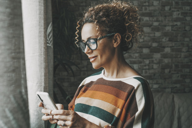 一个快乐的女人在室内对着手机微笑，用应用程序聊天或给人发信息。约会和孤独的生活方式与科技和互联网连接的女性。年轻女士在手机上写字图片下载