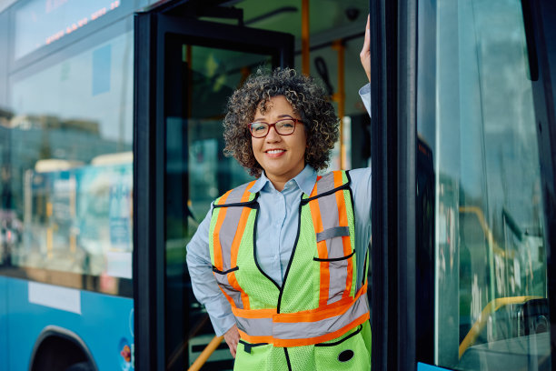 女司机站在公共汽车的入口处，看着摄像头。图片下载