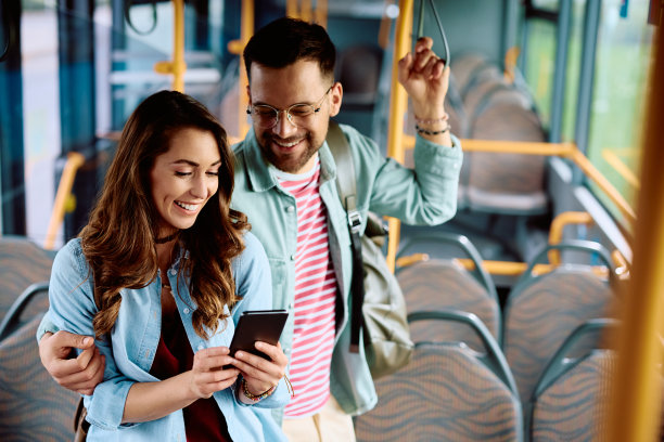 快乐的女人和她的男朋友在公共汽车上用手机。图片下载