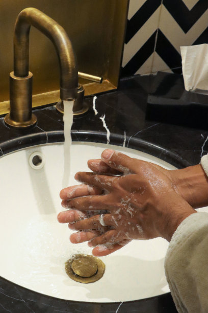 一个面目全非的人站在豪华浴室的水槽前洗手，肥皂，水龙头，黑色大理石浴室柜台，高架的视野，聚焦于前景图片下载