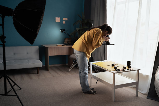 一名身着休闲装的女子在家中工作室用数码相机拍摄创意照片。女摄影师正在拍摄桌子上的美容护肤品。图片下载