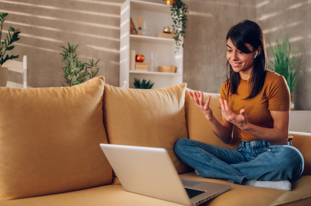 坐在家里黄色沙发上玩笔记本电脑的女人图片下载