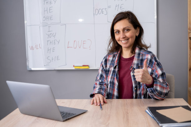 女老师和学生使用笔记本电脑进行在线会议。女教师微笑着翘起大拇指，坐在课桌前，对课堂成绩感到满意图片下载