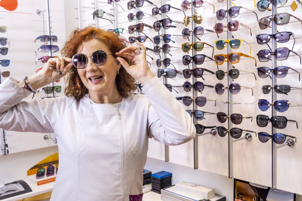 时尚的眼镜:红发验光师在太阳镜展板前试戴太阳镜图片下载