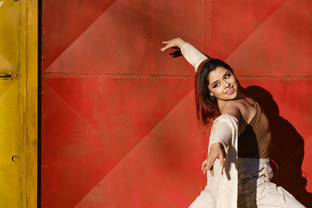 年轻的拉丁女子张开双臂，微笑着以红墙为背景摆出舞蹈姿势。图片下载