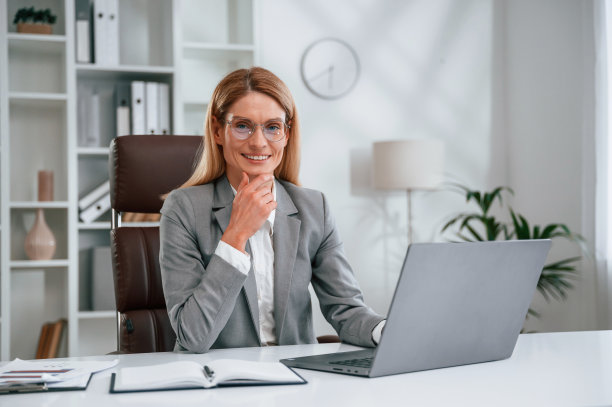 使用笔记本电脑。穿着正装的女士正在办公室工作图片下载