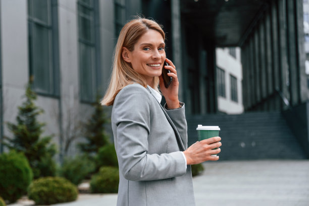 边走边喝，边打电话。一名穿着正装的女子站在商务大楼附近的户外图片下载