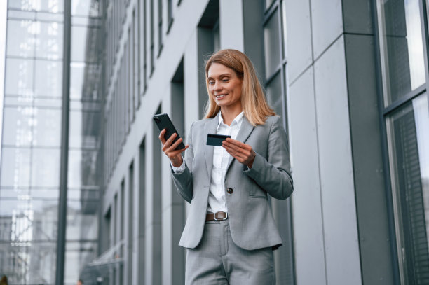 拿着信用卡和智能手机。一名穿着正装的女子站在商务大楼附近的户外图片下载