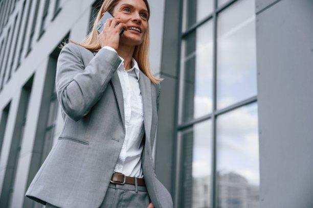 通过电话交谈。一名穿着正装的女子站在商务大楼附近的户外图片下载