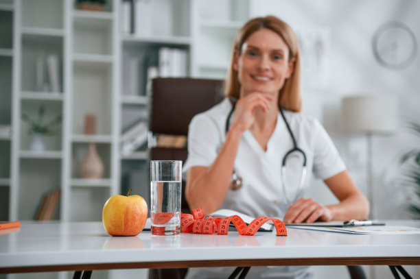 一个苹果和卷尺在桌子上。穿白大褂的年轻女医生在室内图片下载