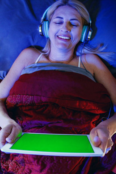 躺在床上微笑着看电子平板电脑的女人图片下载