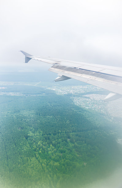 飞机机翼的视图，蓝天和绿色的土地在着陆。飞机窗口视图。图片下载