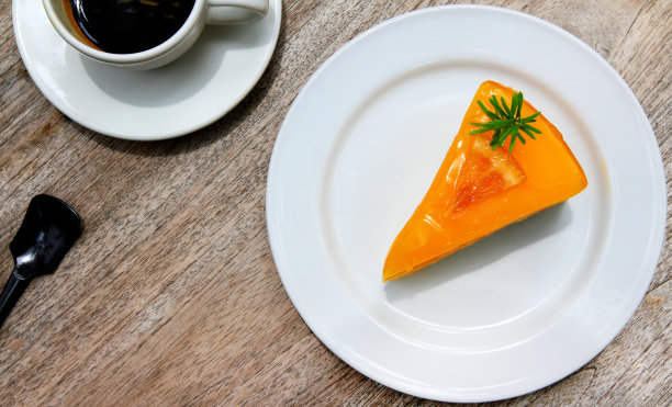 白色盘子或盘子里的一块橙色蛋糕，一杯白色的黑咖啡图片下载