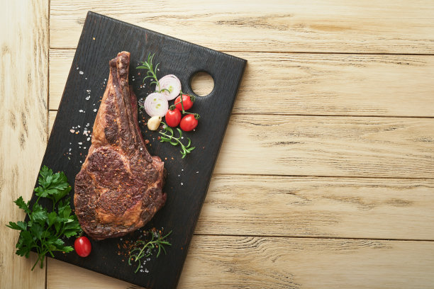 Tomahawk牛排。切成薄片的烤战斧式牛排，配上烤过的圣女果、香草和盐。准备烧烤。俯视图和复制空间。图片下载