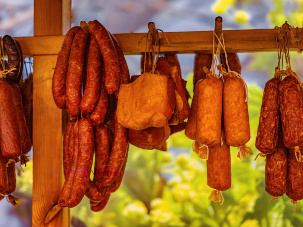 不同种类的自制烟熏干香肠悬挂在深色木制背景上。各种美味的熟食肉，意大利腊肠和意大利香肠图片下载