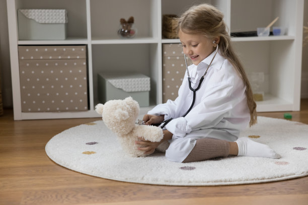 快乐的女孩穿着医学白大褂扮演儿科医生图片下载