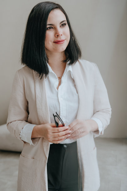 年轻的黑发女商人面带微笑，对着室内明亮的墙壁拿着眼镜图片下载