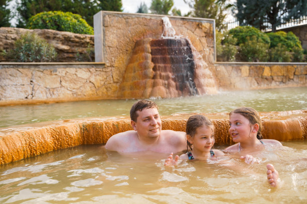 一家人、爸爸和孩子在室外肮脏的温泉里洗澡、游泳。温泉浴池和健康的天然水浴，粘土和黄绿泥。温泉疗养、休闲、家庭度假图片下载