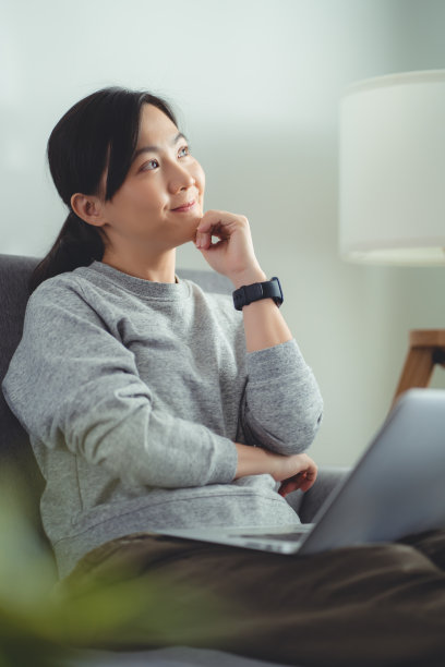 亚洲女性坐在家里的客厅里用笔记本电脑工作或上网。图片下载