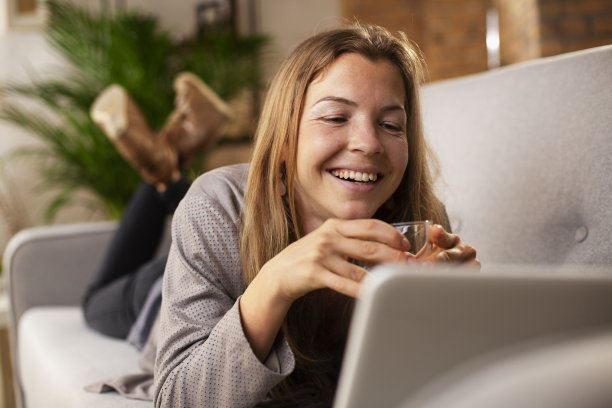 微笑的女孩一边使用笔记本电脑一边喝水图片下载