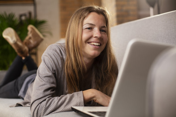 微笑的女孩一边使用笔记本电脑一边喝水图片下载