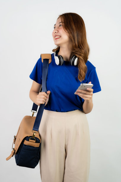 亚洲女学生肩包，戴耳机，手持智能手机白底手机图片下载