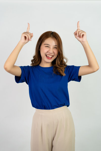 穿着蓝色t恤的快乐亚洲女子双手摆姿势，看着白色背景的相机图片下载