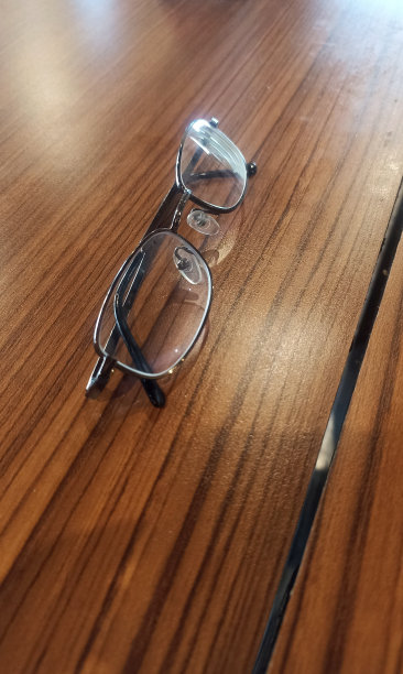 棕色的木桌上放着几副眼镜。黑钛眼镜放在木桌上。办公室的工作场所，在木桌上放着眼镜。钛镜框眼镜。黑色的箱子用于存储。图片下载