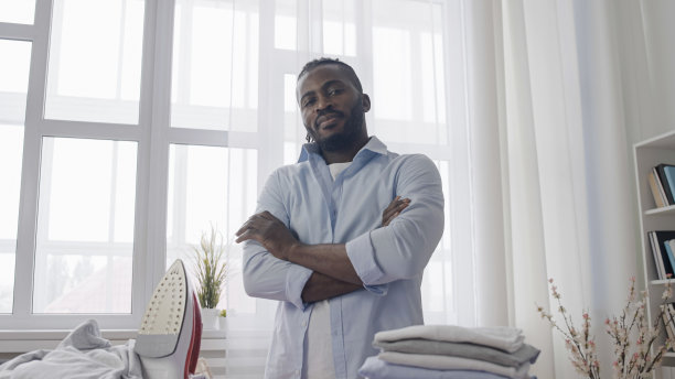 一个年轻人的肖像，拿着一堆刚熨好的衣服，做家务图片下载