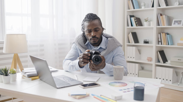 一位男艺术家正在调整他的新专业相机，并在他的笔记本电脑上观看教程图片下载