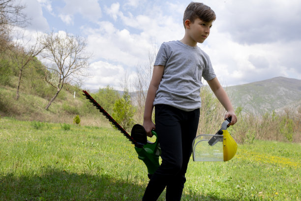 一个男孩带着园艺设备修剪器和带面罩的安全帽图片下载