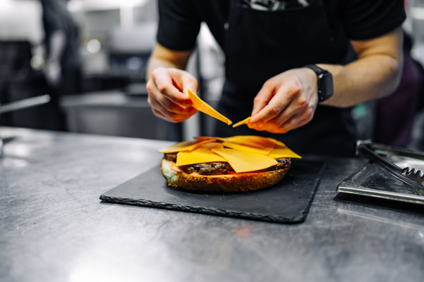 厨师在餐厅的厨房里用手烹饪超大的芝士汉堡。一步一步地图片下载