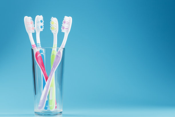 不同颜色的牙刷放在蓝色背景的透明玻璃里。图片下载