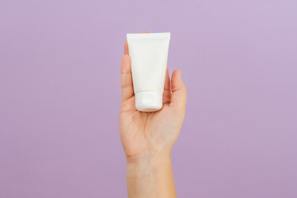女人手里的化妆霜管，以丁香为背景。美丽的概念。化妆品包装管图片下载