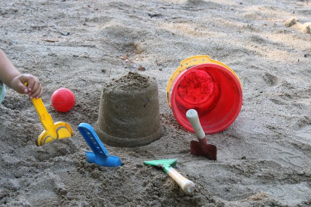 一个孩子拿着一把黄铲子在沙滩上玩耍。夏天的时间。海滩上孩子们的玩具图片下载