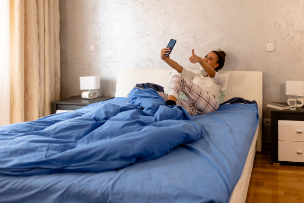一张年轻美女躺在床上用智能手机视频通话的照片。图片下载
