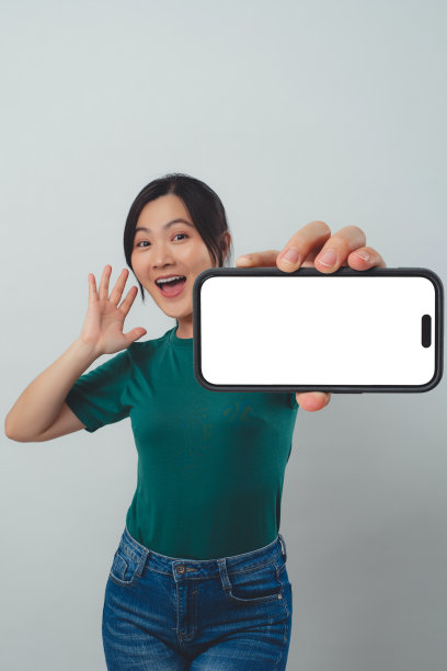 亚洲女子开心地微笑着，在智能手机上显示白色屏幕，孤立地站在背景中。图片下载